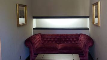 A room with a tufted red sofa, two striped chairs, a small table, and a hanging light fixture.