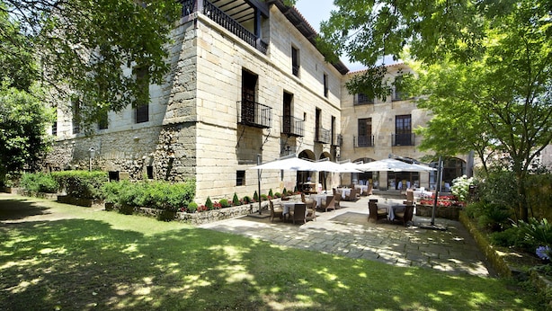 A courtyard with stone buildings, outdoor seating, and greenery. - Parador De Santillana De Gil Blas (Santillana del Mar)