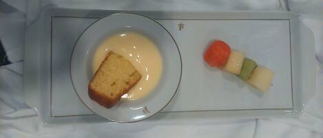 Un plato de postre con una porción de pastel y un pincho de frutas sobre una bandeja.