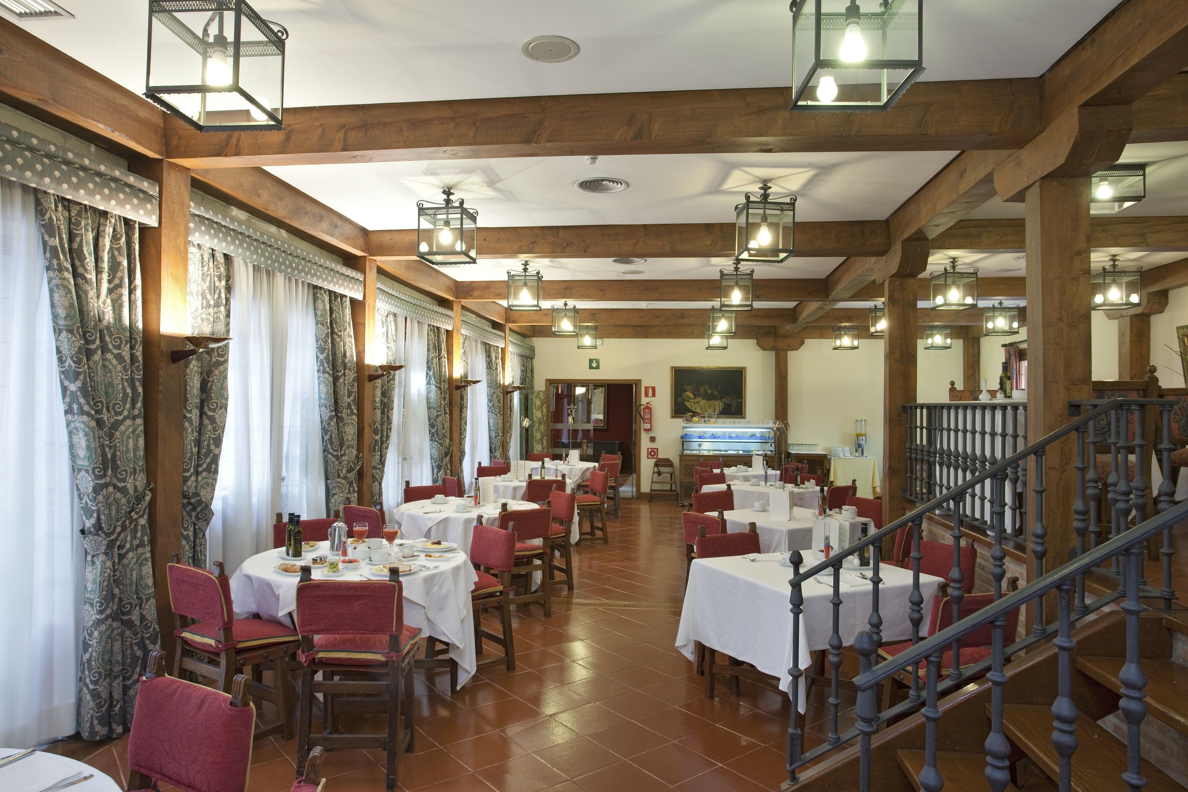 A dining area with tables and chairs, wooden beams, and hanging lanterns.