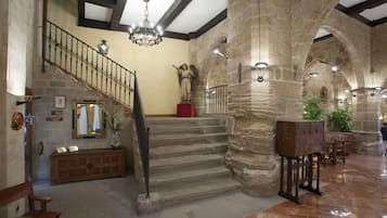 A grand staircase with stone walls and a wooden floor, leading to a landing with a statue and a mirror.