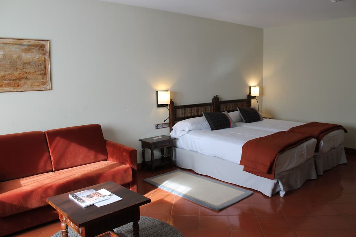 Une chambre d’hôtel avec un lit, un canapé, une table de chevet et un tableau au mur.