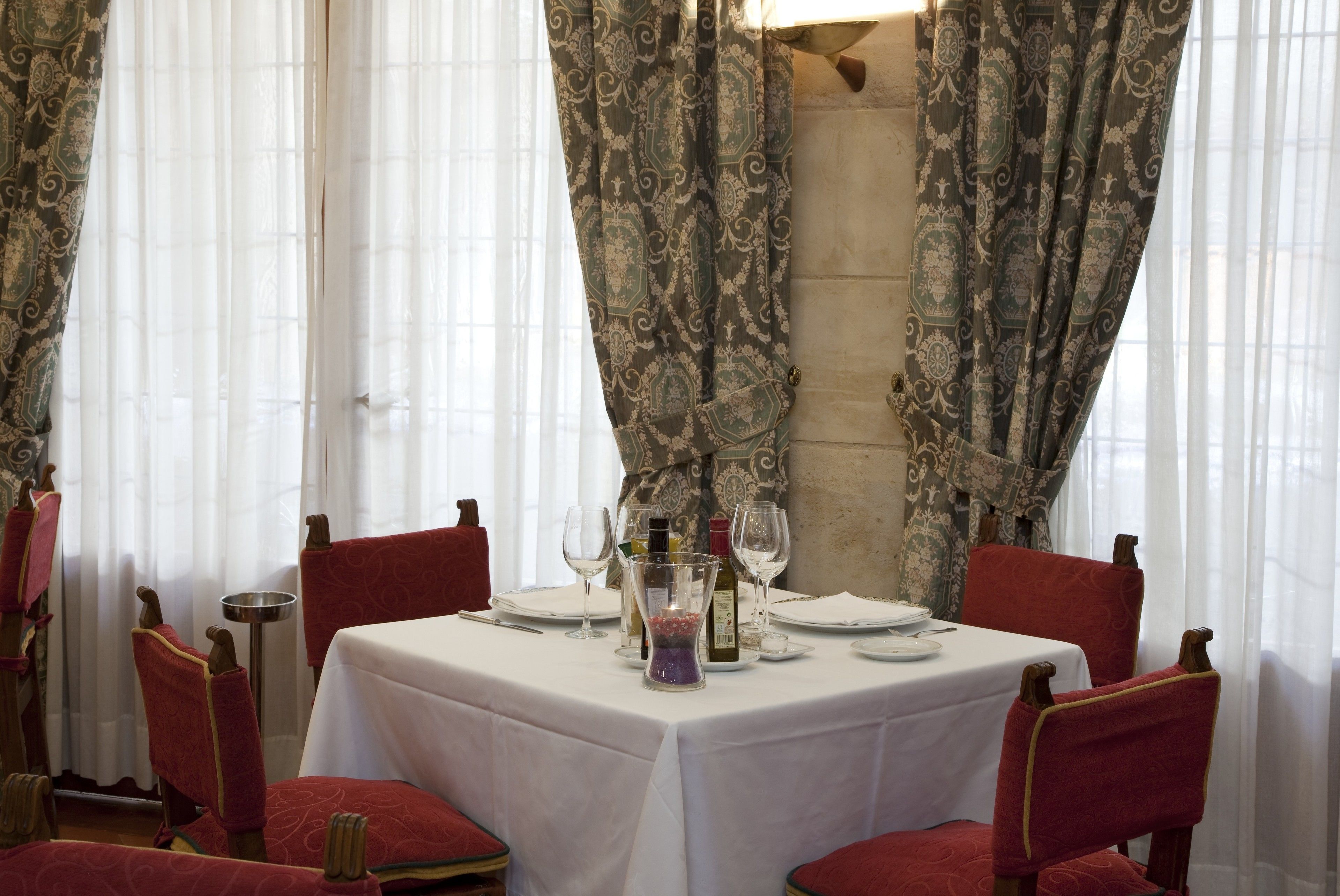 A dining table set with white tablecloth, red chairs, and wine glasses.