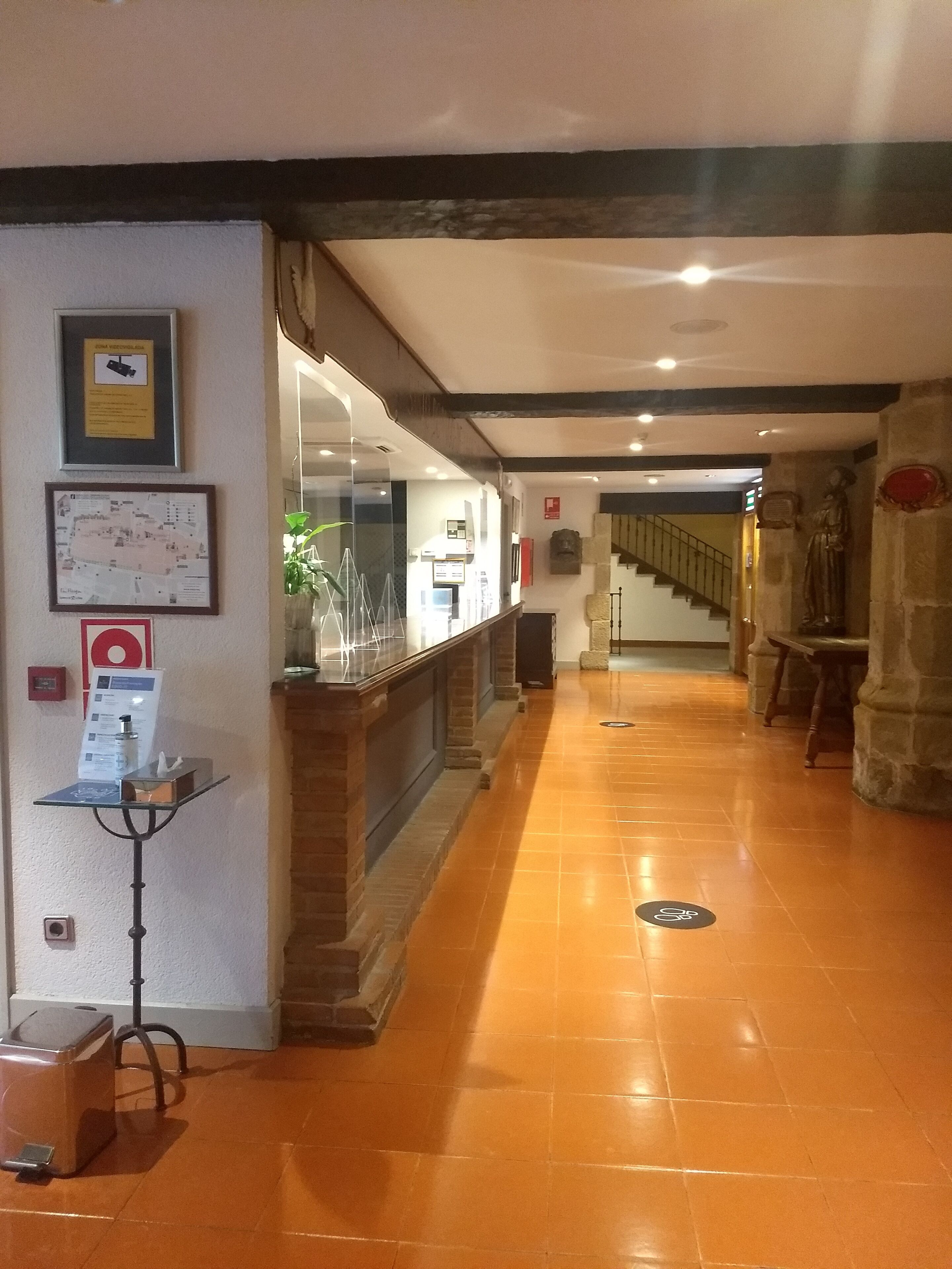 A hotel lobby with a reception desk, a map, and a staircase leading to another floor.