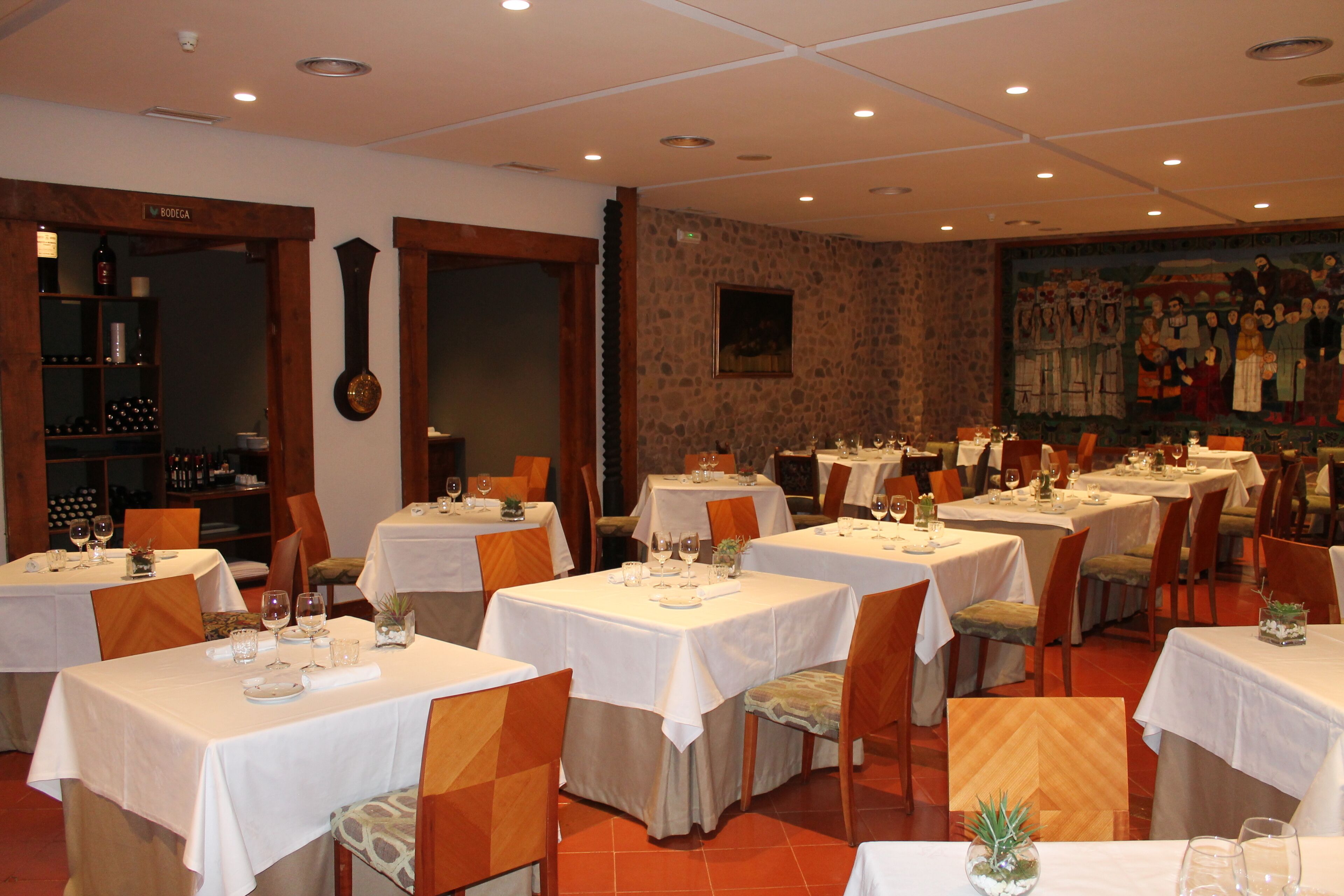 Un restaurante con varias mesas y sillas, una estantería para vinos y un mural en la pared.