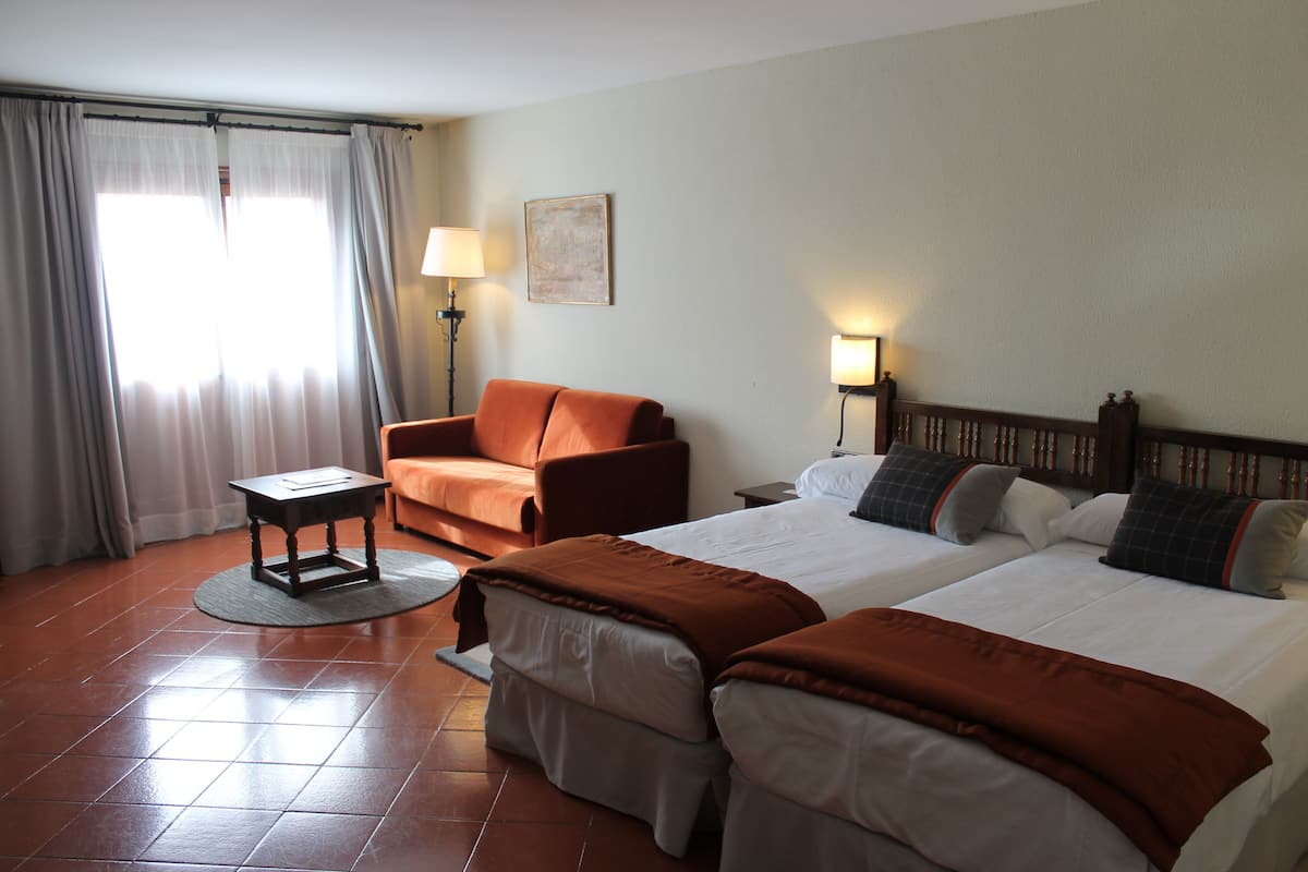 Une chambre d’hôtel avec deux lits, un canapé, une petite table et une lampe.