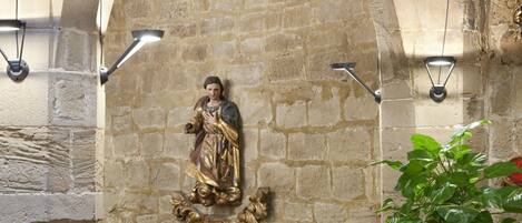 Interior de paredes de piedra con una estatua, un armario de madera, una lámpara y una planta en maceta.