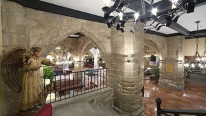 A stone-walled interior with a staircase, a chandelier, and a statue of an angel. - Parador de Santo Domingo de la Calzada (Santo Domingo de la Calzada)