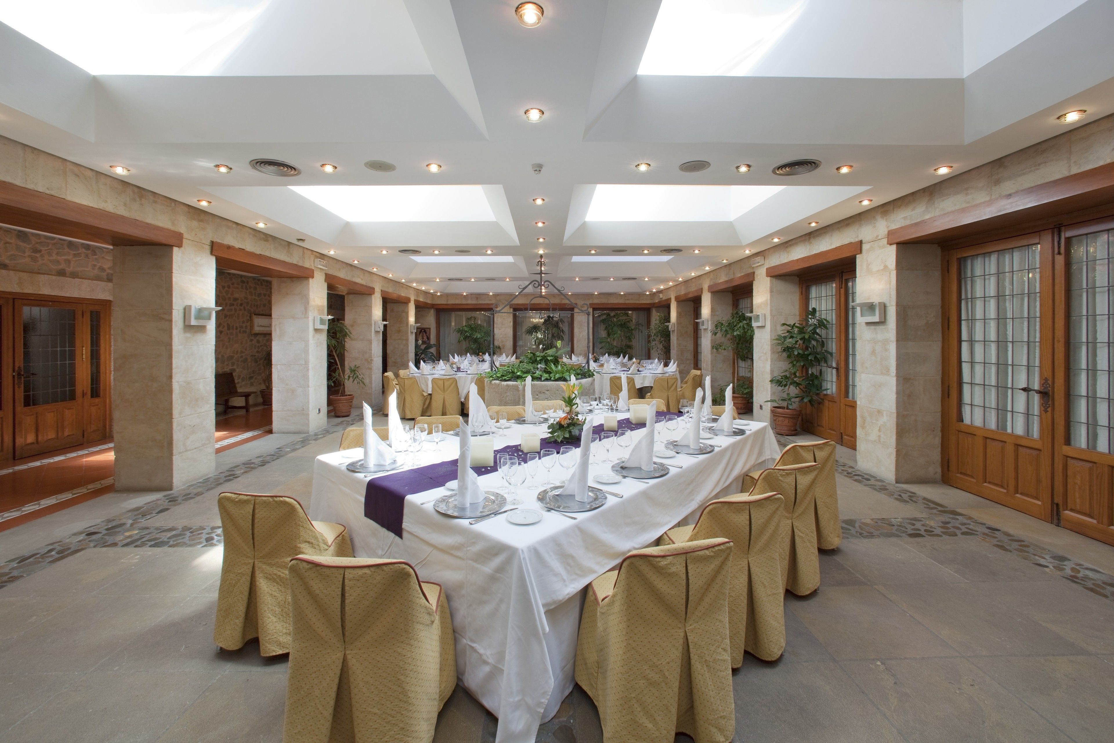 A banquet hall with a long table set for a formal event, flanked by tall columns and large windows.