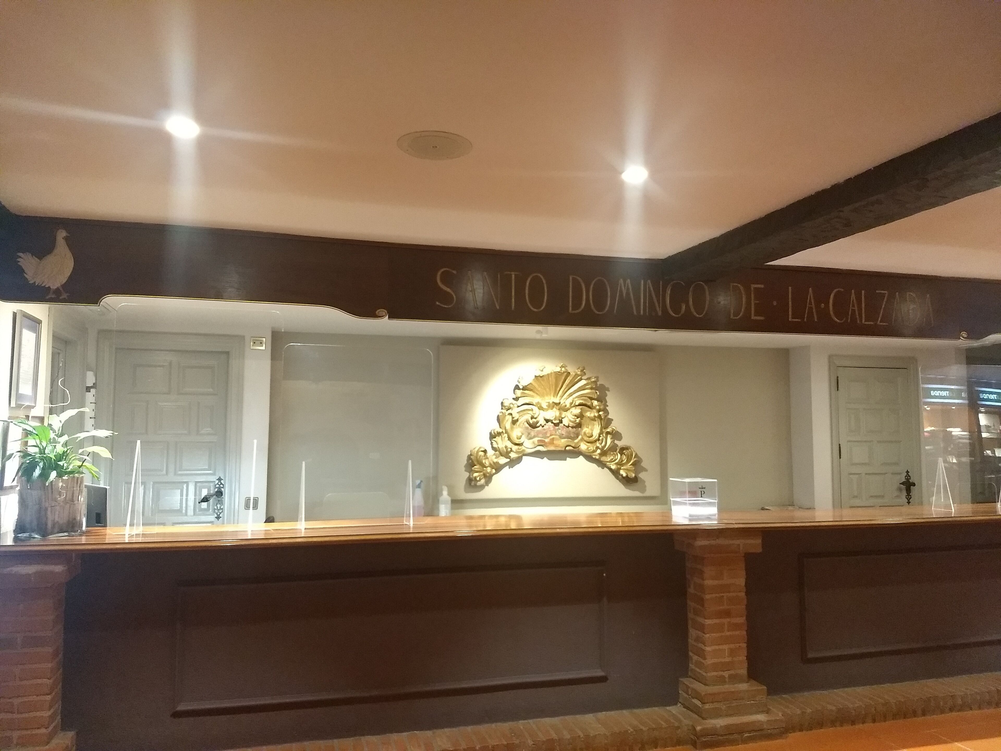 A reception desk with a decorative emblem above it and a sign above the desk that reads "SANTO DOMINGO DE LA CALZADA".