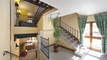 Un interior con varios niveles, una escalera, una planta en maceta, una estatua y un ventanal con cortinas.