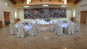 Un salón de banquetes con mesas redondas dispuestas para un evento formal, con un gran cuadro abstracto en la pared de fondo.