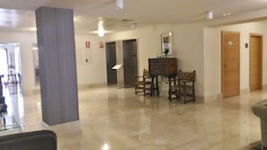 A hotel lobby with a polished floor, a reception desk, two wooden doors, and a wall-mounted fire alarm.