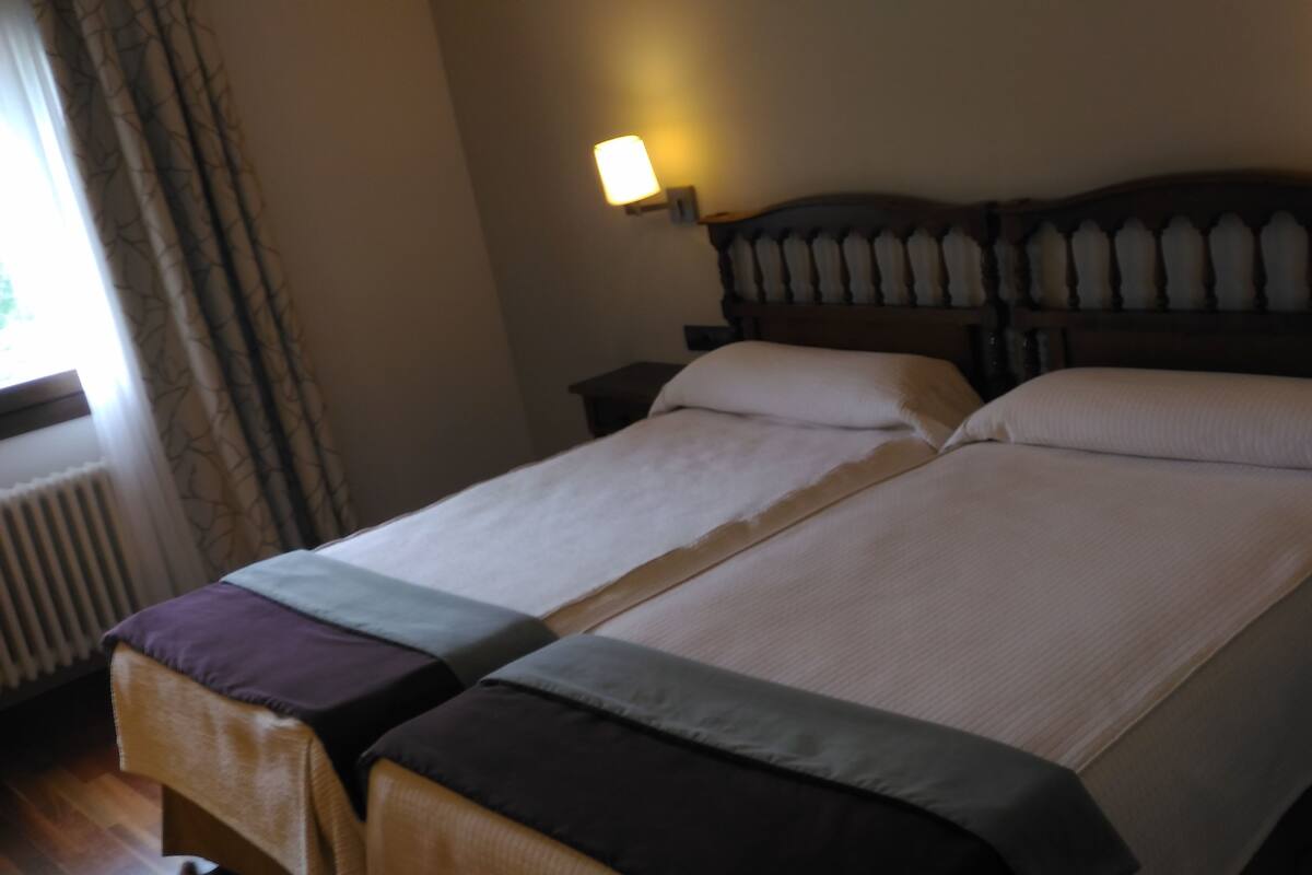 A double bed with a wooden headboard, two bedside tables, and a window with curtains.