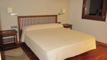 A neatly made bed in a room with wooden flooring, two bedside tables, and wall-mounted lamps.