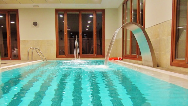 An indoor swimming pool with clear water, a water fountain, and wooden-framed windows.