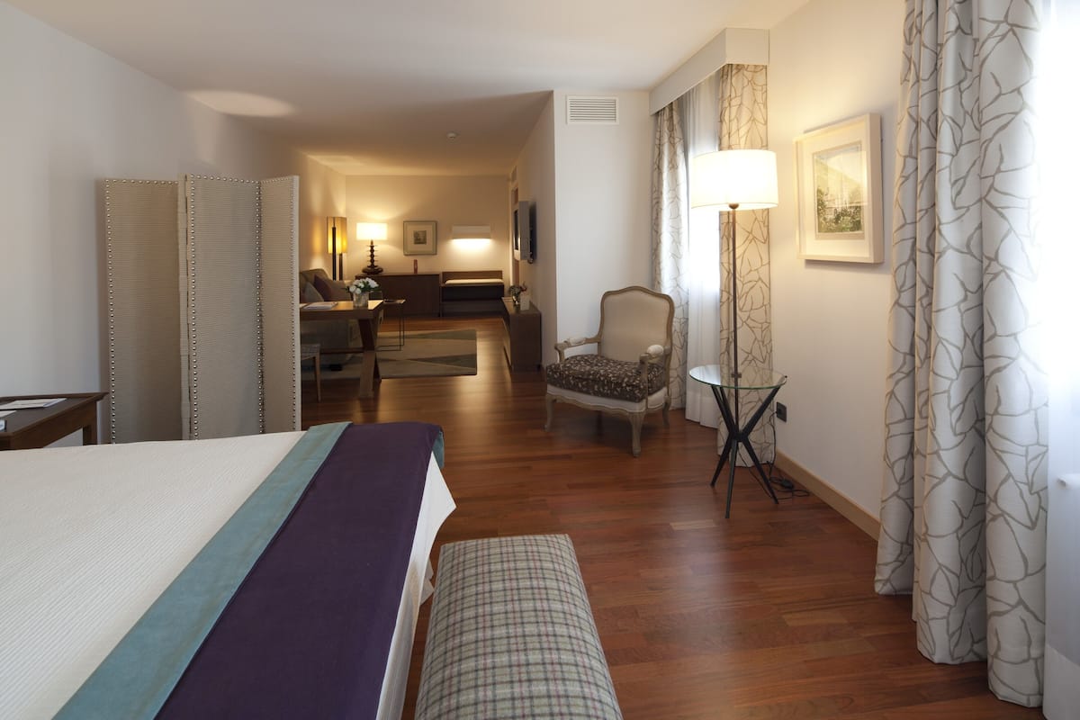 A hotel room with a bed, a chair, a small table, and a sofa.