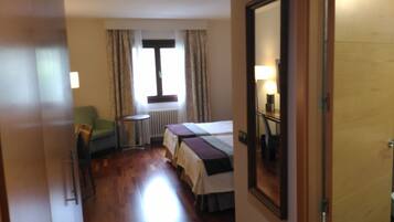 Habitación de hotel con cama, una silla, una mesita y una ventana con cortinas.
