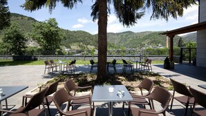 An outdoor seating area with wicker chairs and tables, a large tree, and a view of a hillside.