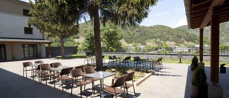 An outdoor patio with tables and chairs, surrounded by trees and a view of hills.