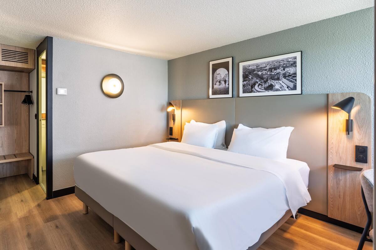 Habitación de hotel con una cama, un armario, un espejo y dos cuadros en la pared.