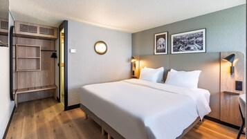 Habitación de hotel con una cama, un armario, un espejo y dos cuadros en la pared.