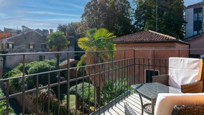 Un balcón con vistas a un jardín, una silla de mimbre y una mesa.
