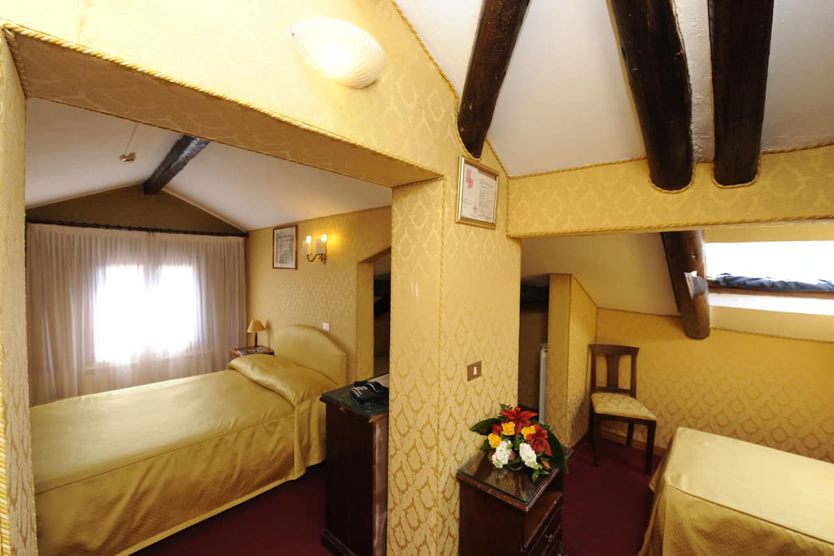 A room with two beds, a desk, a chair, and a small table with a vase of flowers.