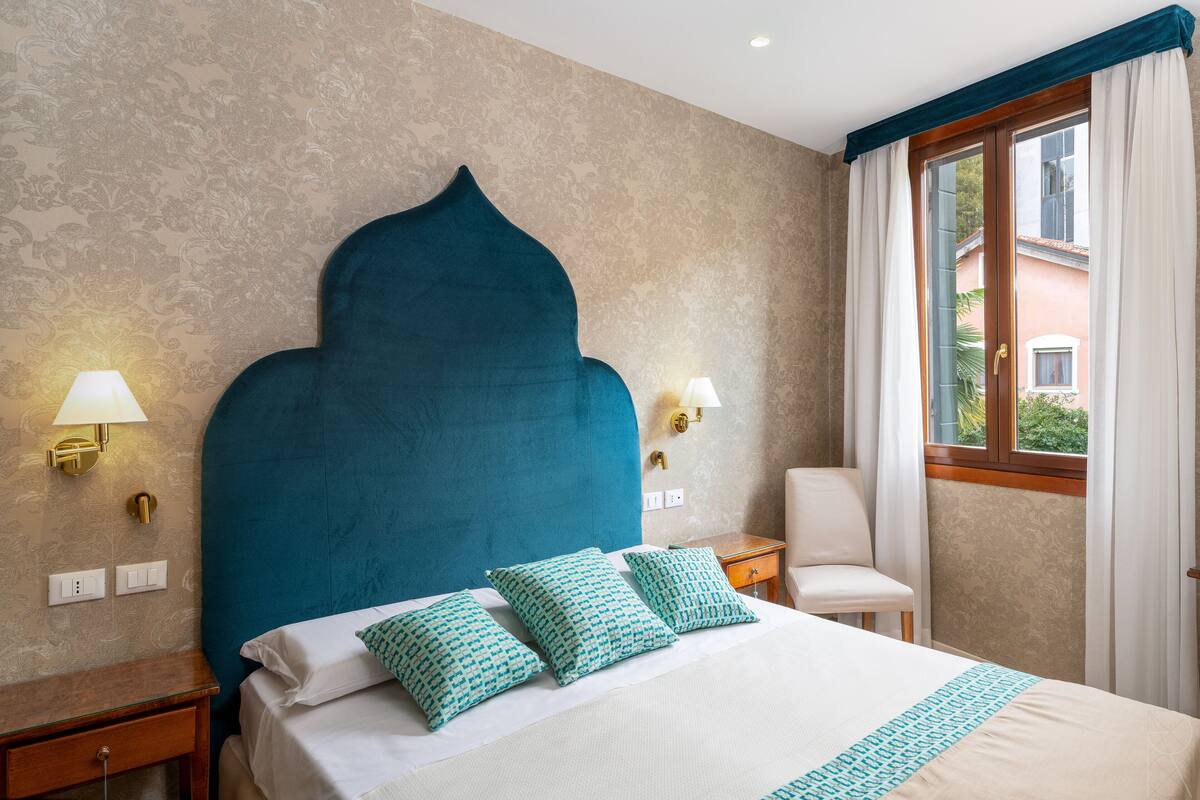 A hotel room with a large bed, two bedside lamps, a chair, and a window with curtains.