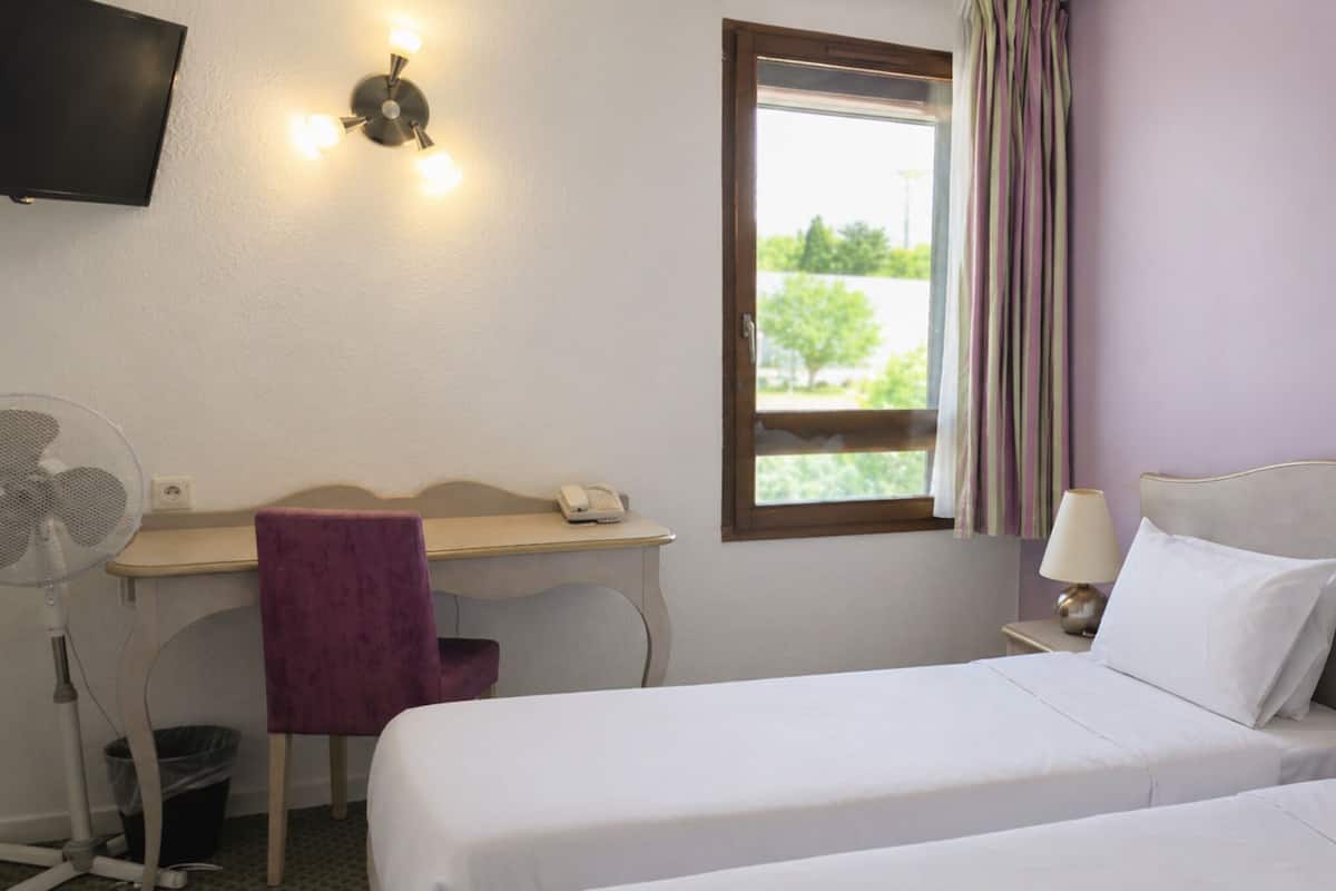 A hotel room with two beds, a desk, a chair, a TV, and a window with curtains.