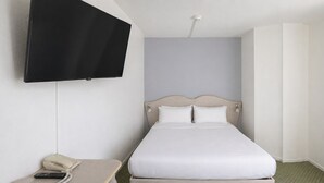 Una cama individual con cabecera, una mesita de noche con teléfono y un televisor montado en la pared.
