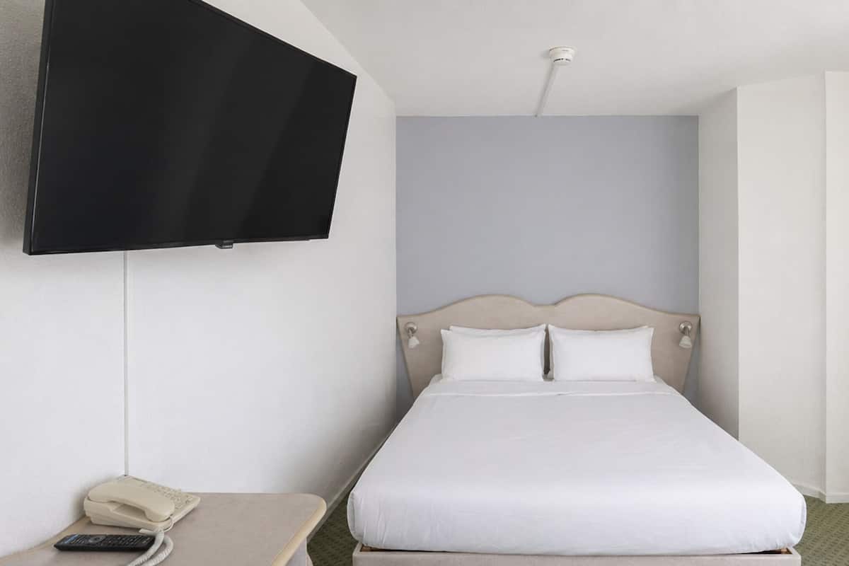 A single bed with a headboard, a bedside table with a telephone, and a wall-mounted television.