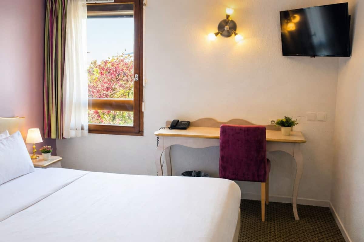 A hotel room with a bed, a desk, a chair, a TV, and a window with curtains.