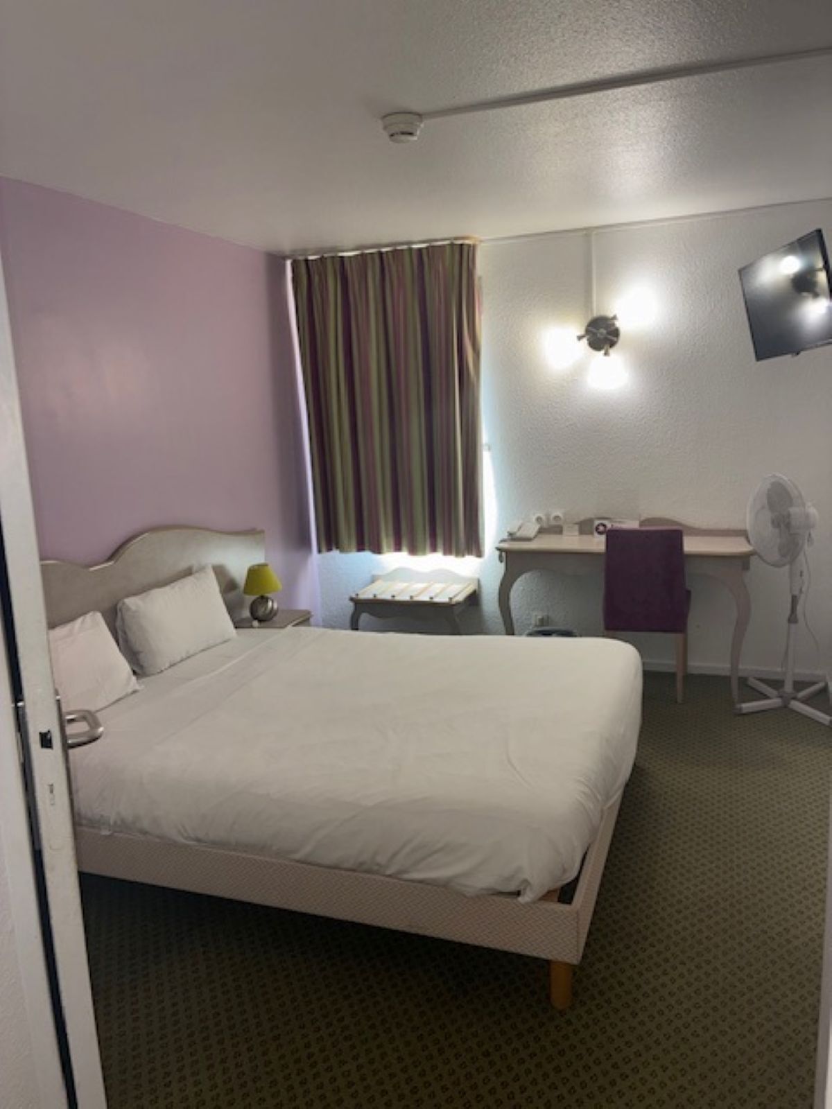 Habitación de hotel con cama, escritorio, silla, televisión y ventana con cortinas.