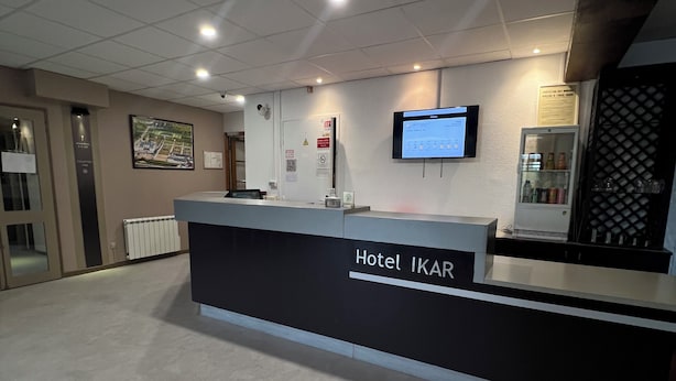 Un mostrador de recepción de hotel con una pantalla digital, un refrigerador y un televisor montado en la pared.