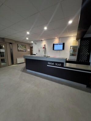 A hotel reception desk with a digital screen, a refrigerator, and a wall-mounted TV.