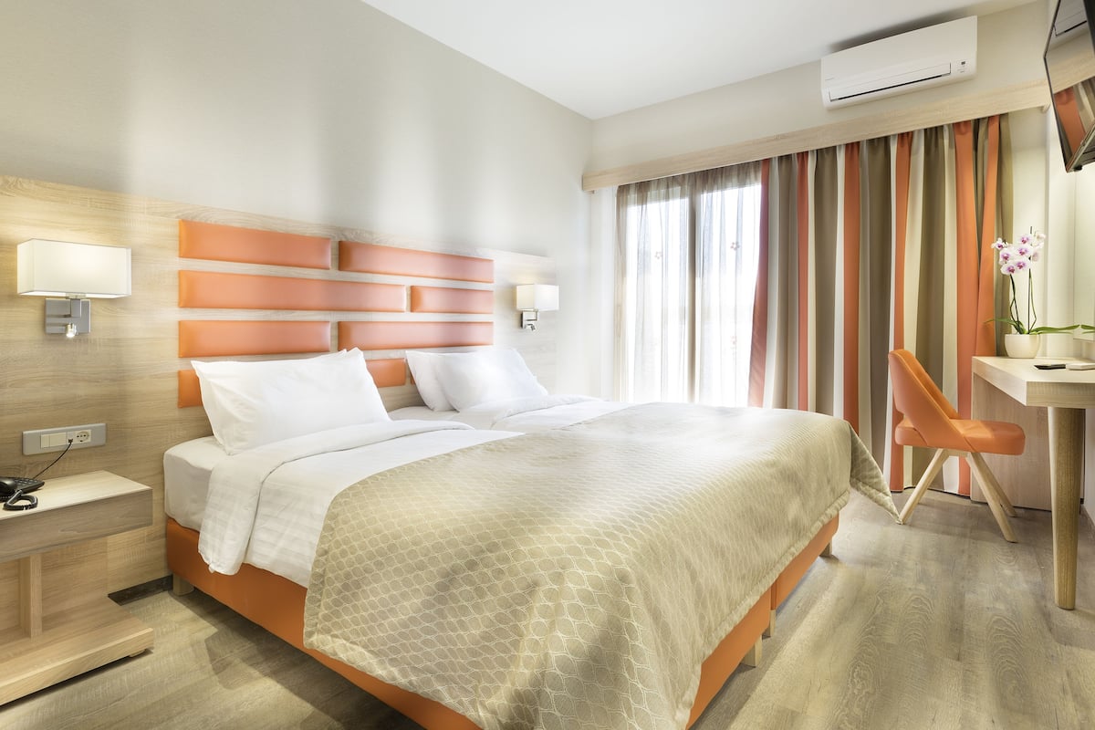 Habitació d'hotel amb llit, taula de nit, làmpada i escriptori amb cadira.