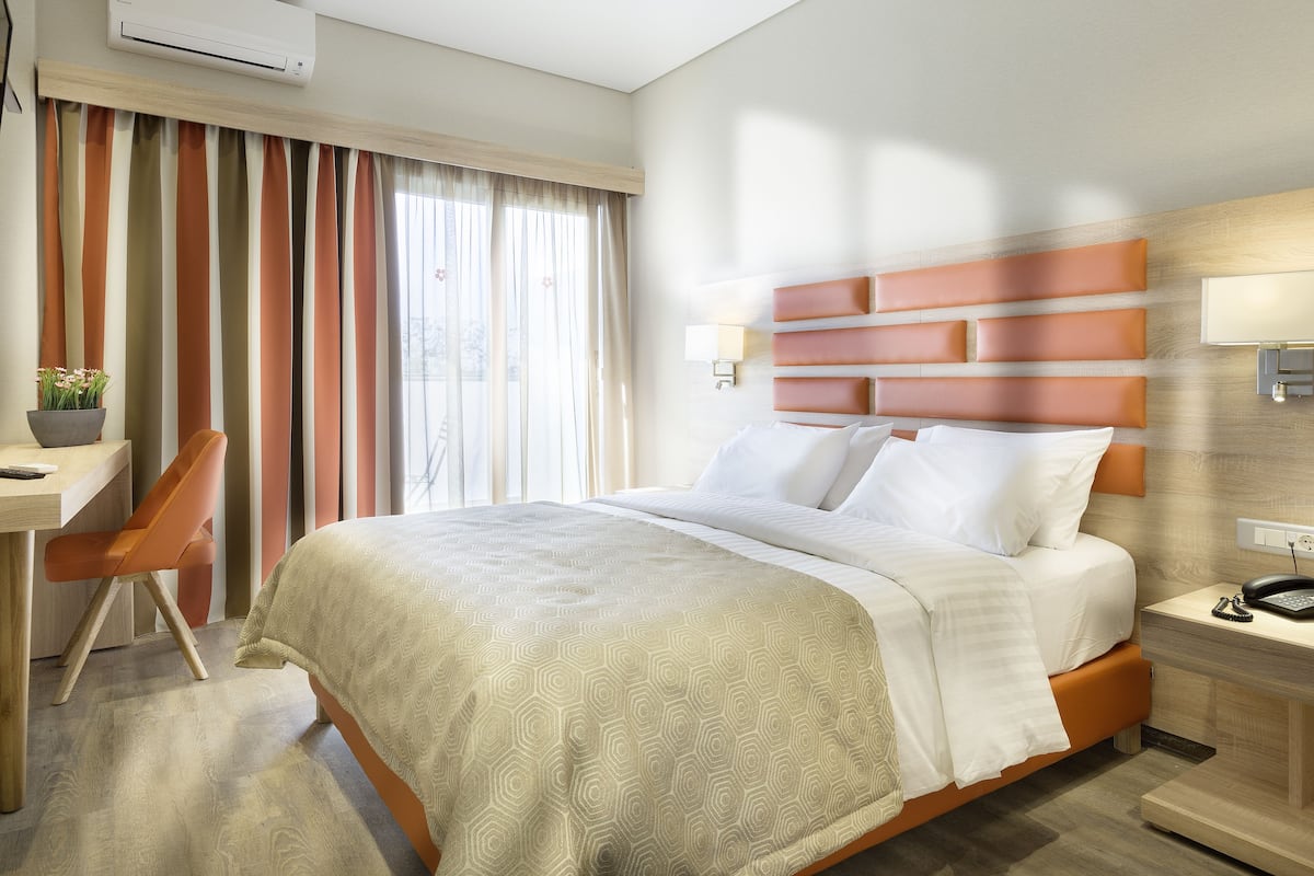 Habitació d'hotel amb un llit gran, un escriptori amb cadira, una taula de nit amb una làmpada i una finestra amb cortines.