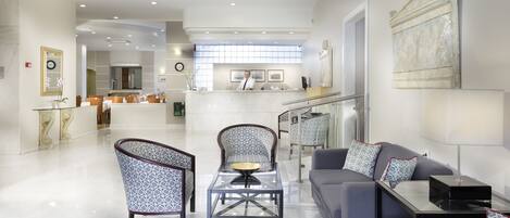 A spacious hotel lobby with a reception desk, seating area with patterned chairs, a sofa, and a coffee table.