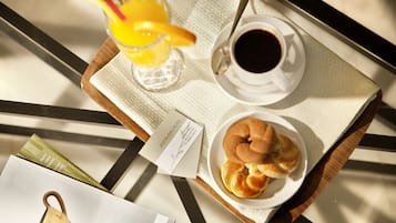 A breakfast tray with a cup of coffee, a glass of orange juice, and a plate of pastries on a table.