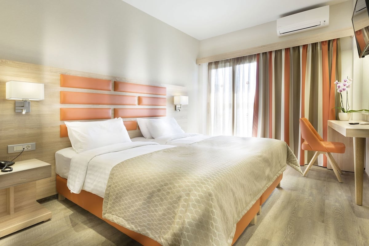 Habitació d'hotel amb llit, taulell de nit, làmpada, escriptori, cadira i aire condicionat.