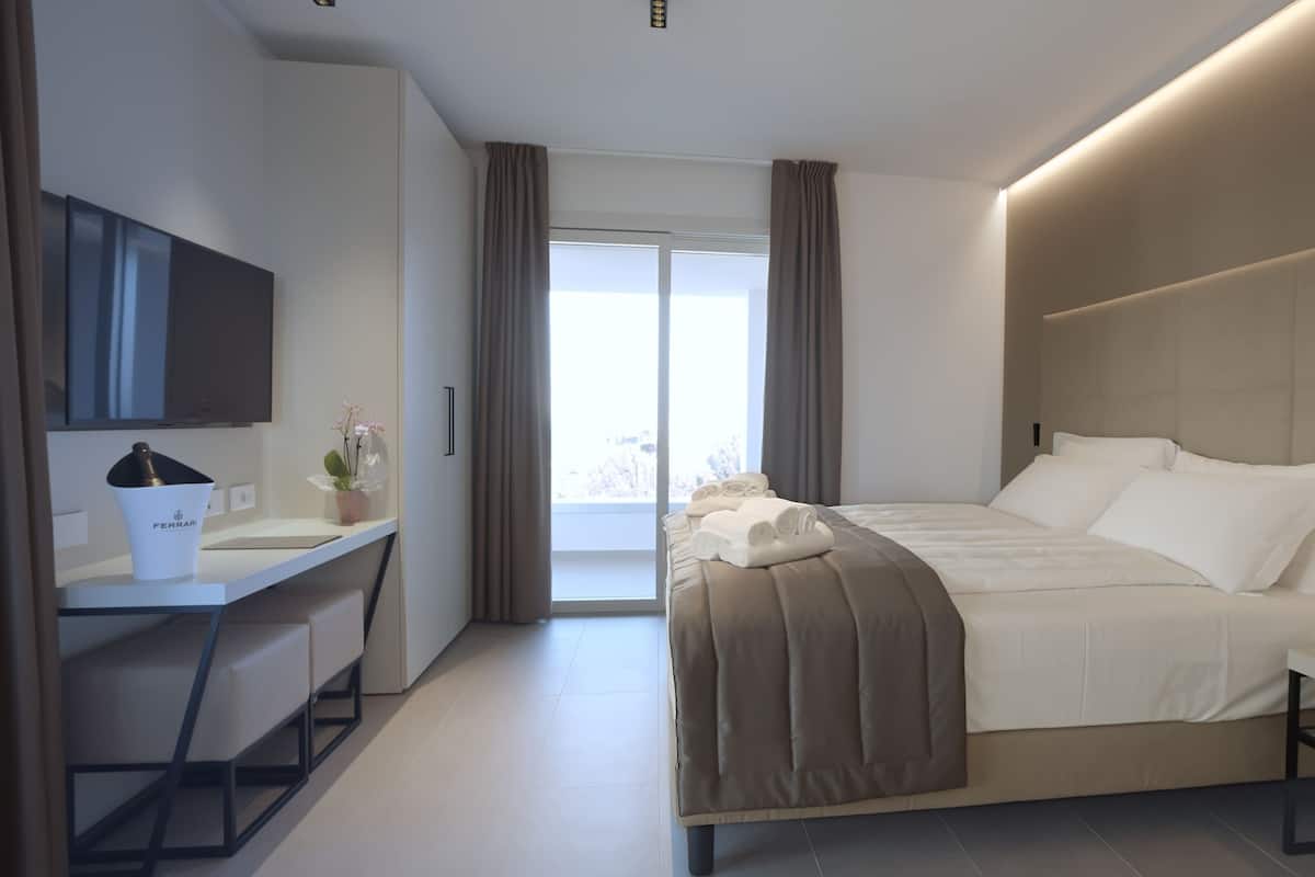 A modern hotel room with a bed, desk, and a large window.