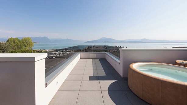 A rooftop terrace with a hot tub, a clear view of the sea, and distant mountains. - Hotel Cristal (Sirmione)