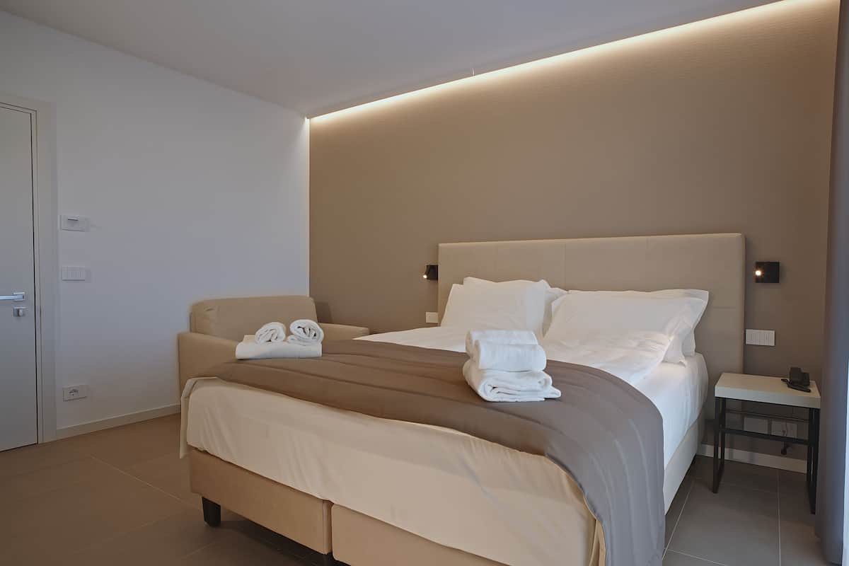 A modern hotel room with a large bed, a bedside table, and a wall-mounted light.