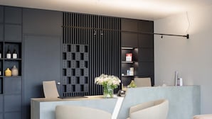 A modern reception area with a desk, two chairs, a wall-mounted number board, and shelves with items. - Hotel Cristal (Sirmione)