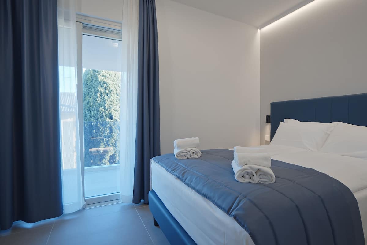 A hotel room with a bed, a view through a window, and a door.