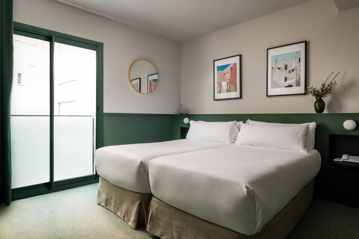 A double bed with a green headboard, a round mirror, and two framed pictures on the wall.