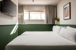 Quarto de hotel com cama, televisão, janela com cortinas e um quadro na parede.