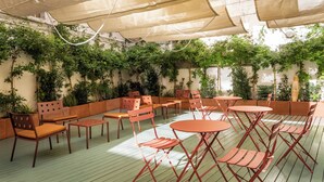 An outdoor seating area with tables and chairs, surrounded by greenery and covered by large umbrellas. - BYPILLOW Mothern (Barcelona)