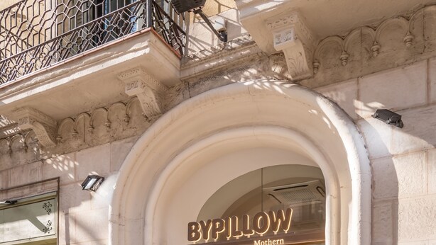 A boutique hotel entrance with an arched doorway, a sign reading "By Pillow Mothern," and a visible interior with a sofa and a mirror. - BYPILLOW Mothern (Barcelona)